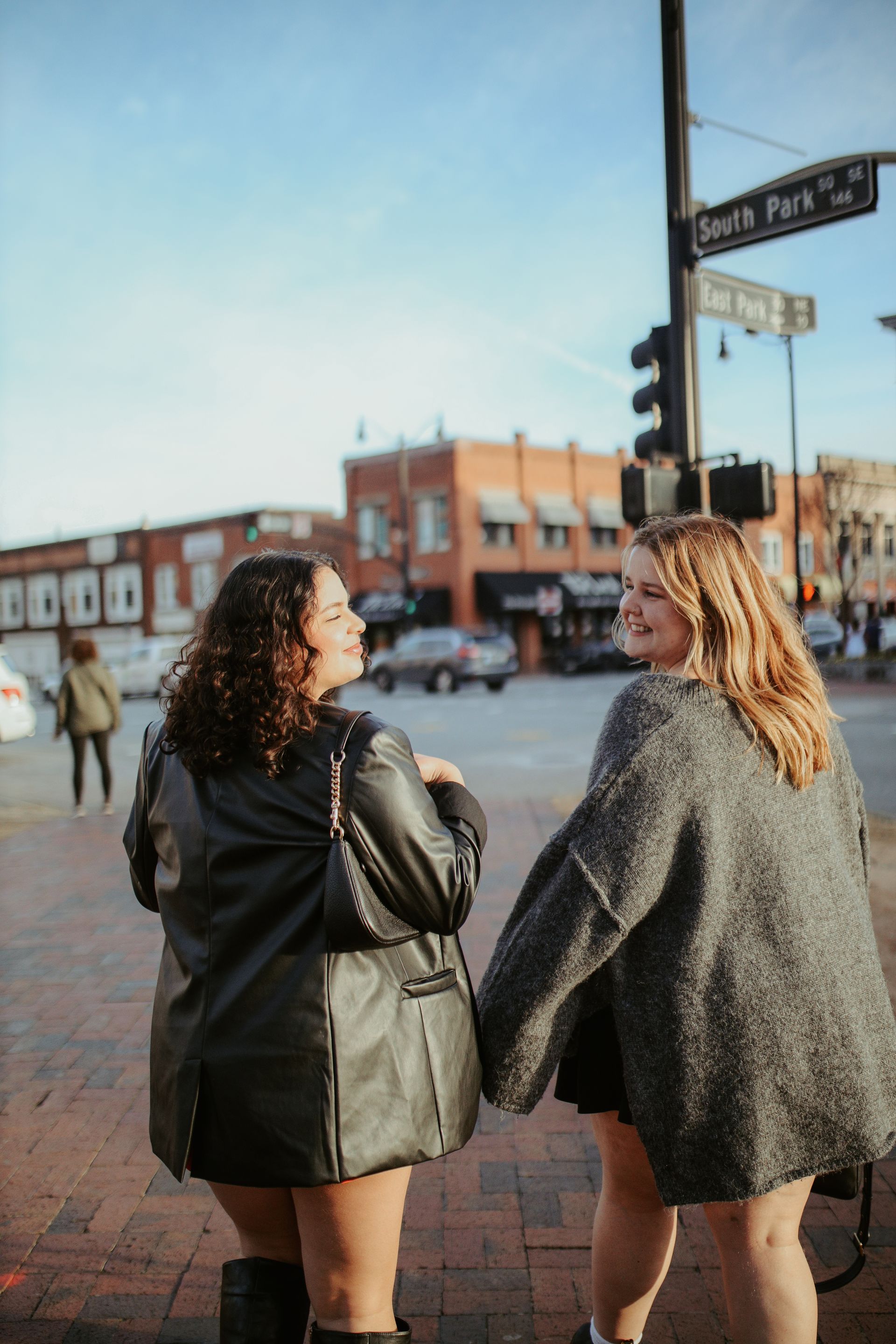 Two women are standing next to each other on a sidewalk holding hands.