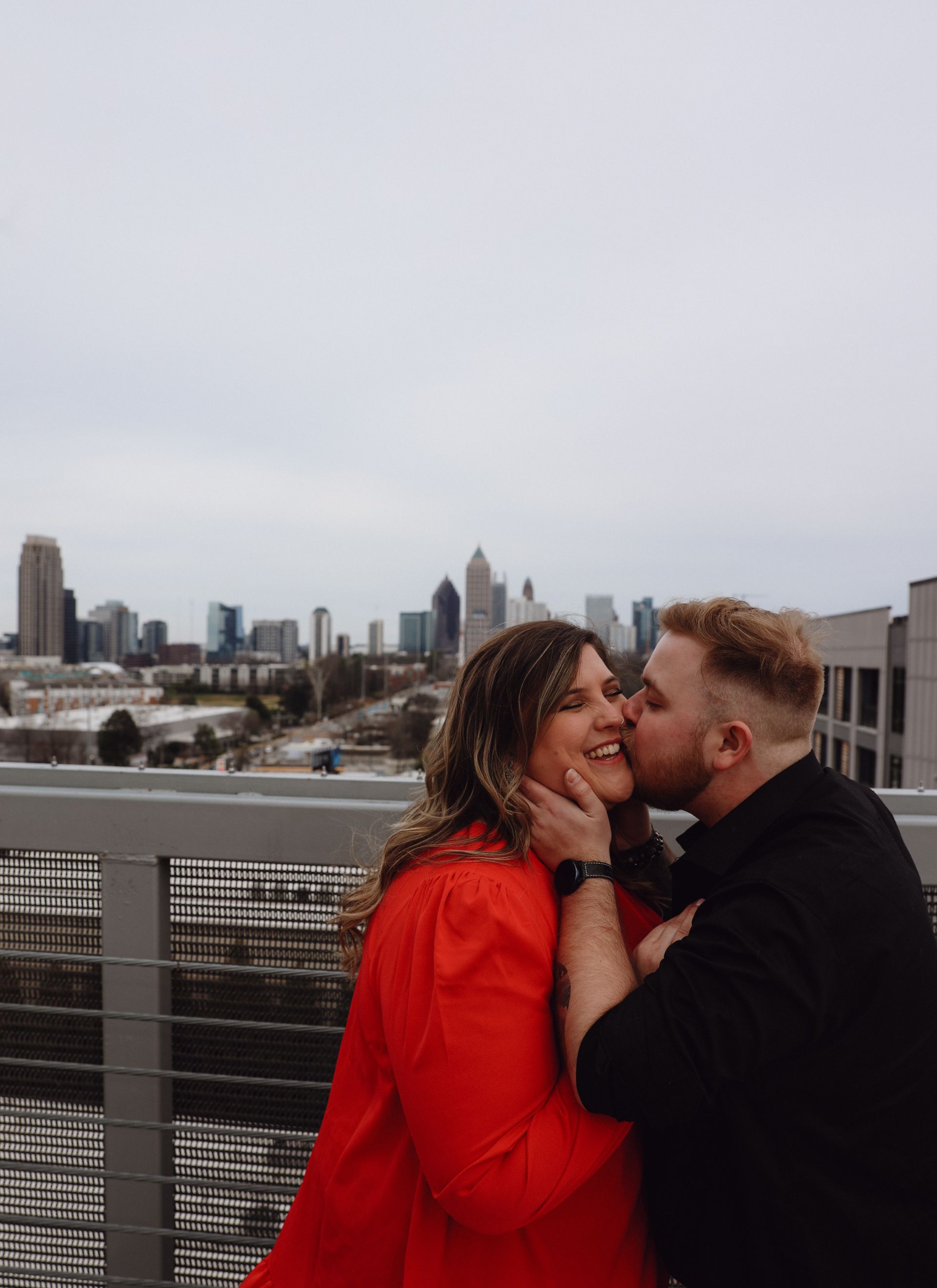 A man is kissing a woman on the cheek on a bridge.