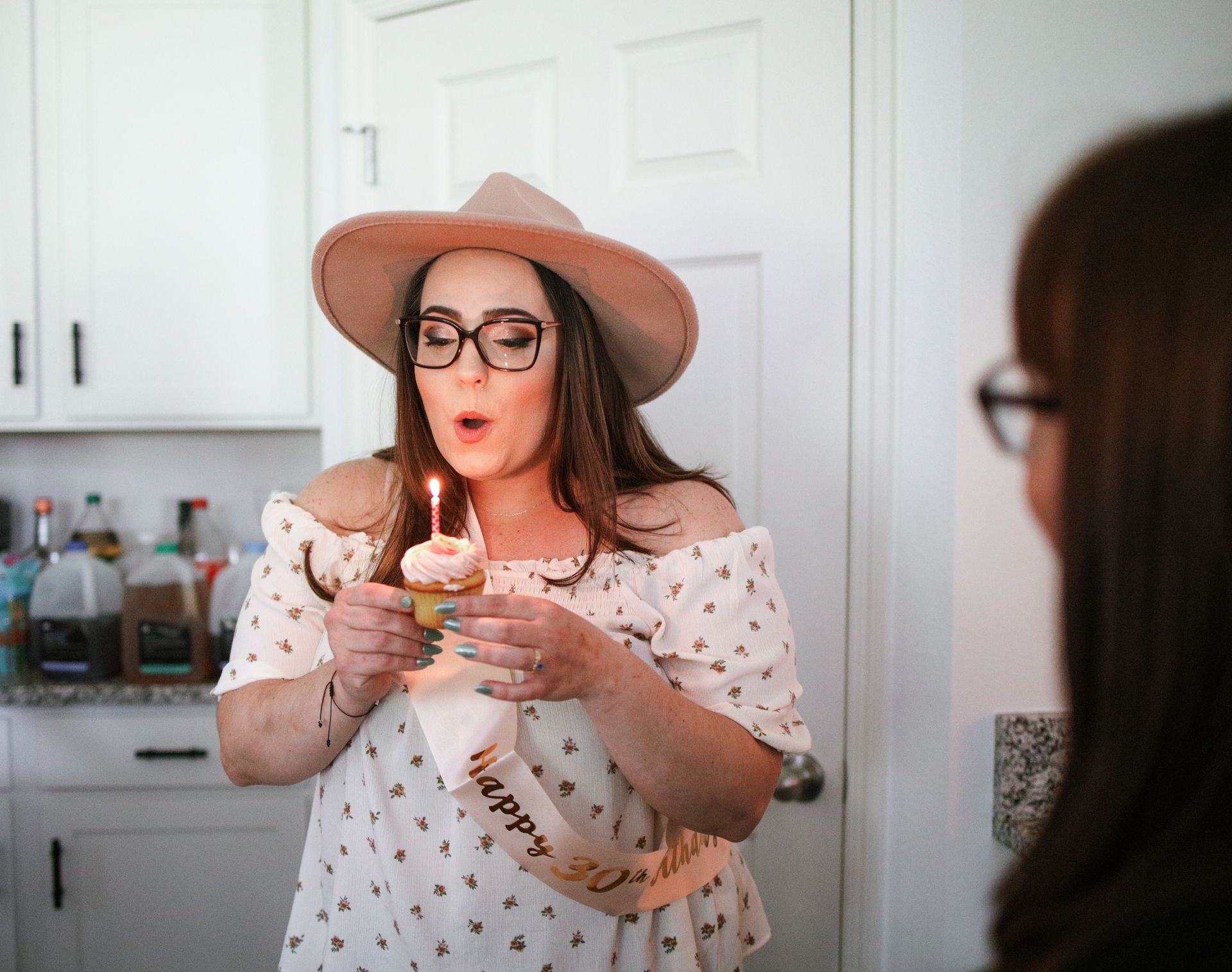 A woman is blowing out a candle on a cupcake.