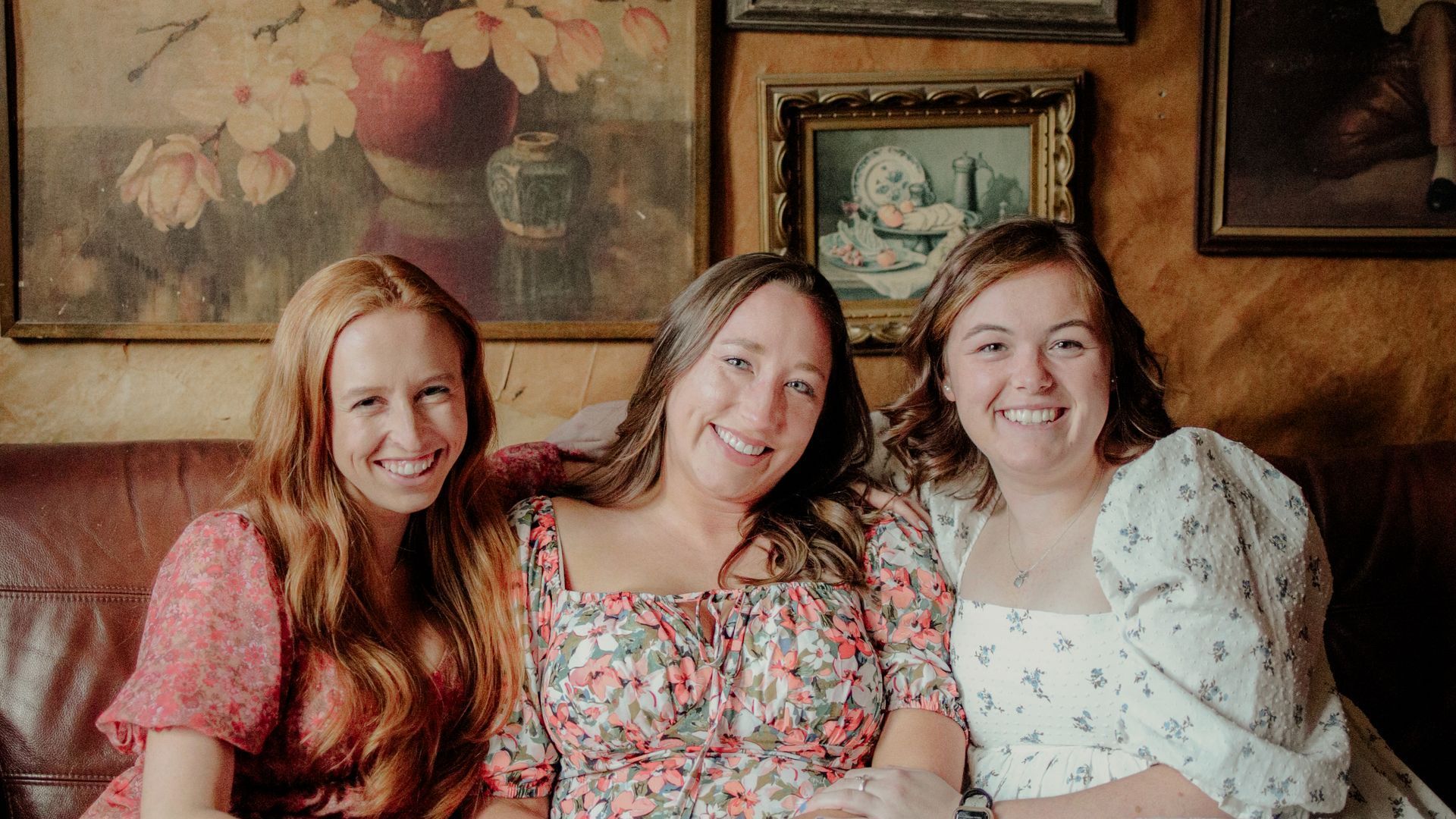Three women are posing for a picture while sitting on a couch.