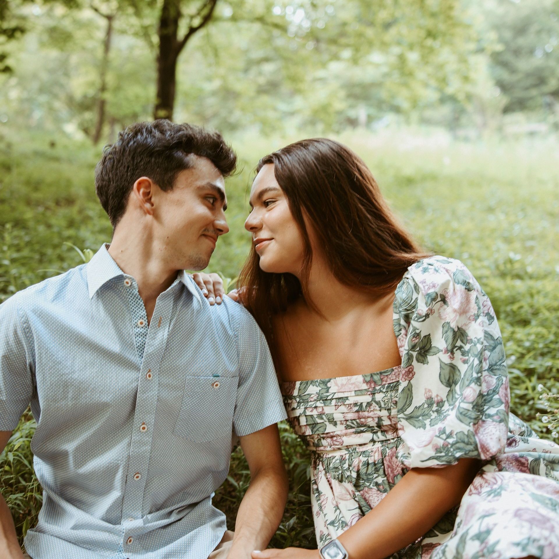 A man and a woman are sitting in the grass looking at each other.
