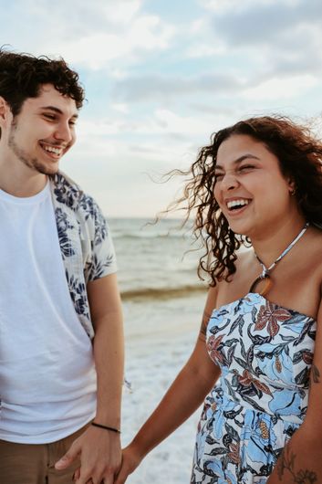 A man and a woman are holding hands on the beach and smiling.