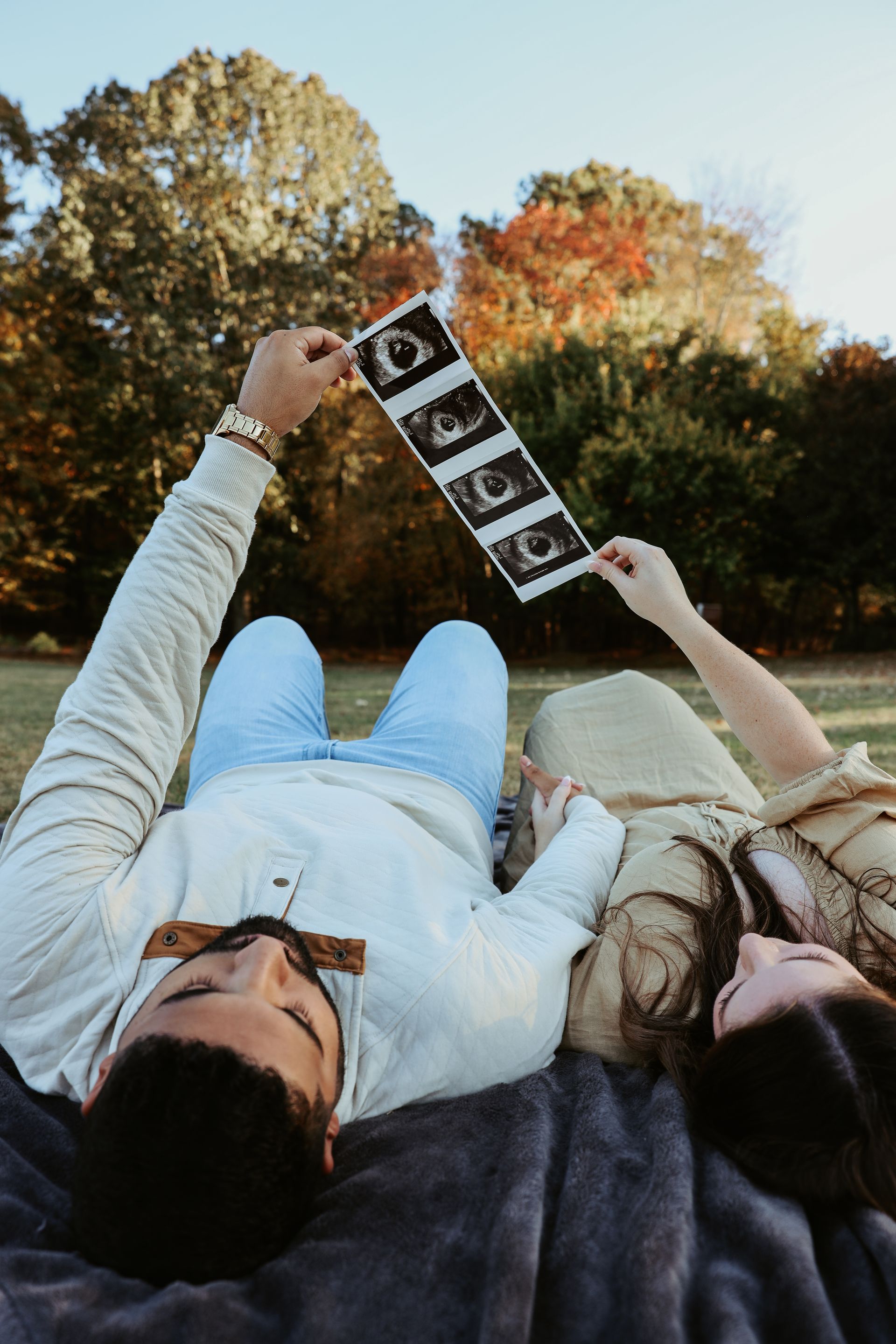 A man and a woman are laying on a blanket holding an ultrasound.