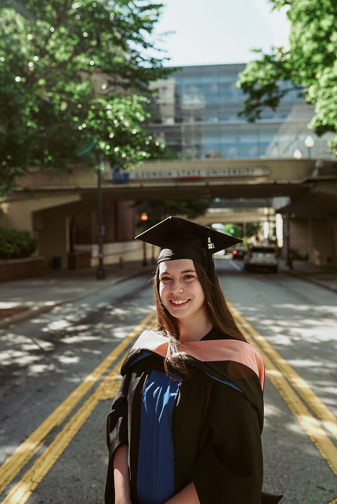 A woman in a graduation cap and gown is standing in the middle of a street.