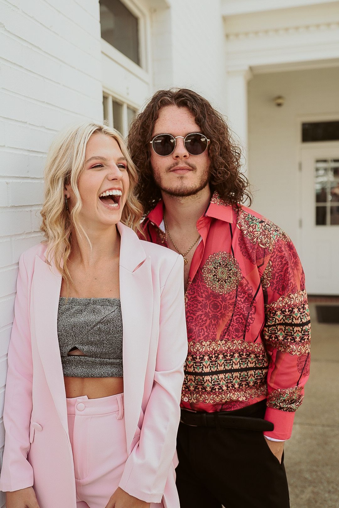 A man and a woman are standing next to each other in front of a white building.