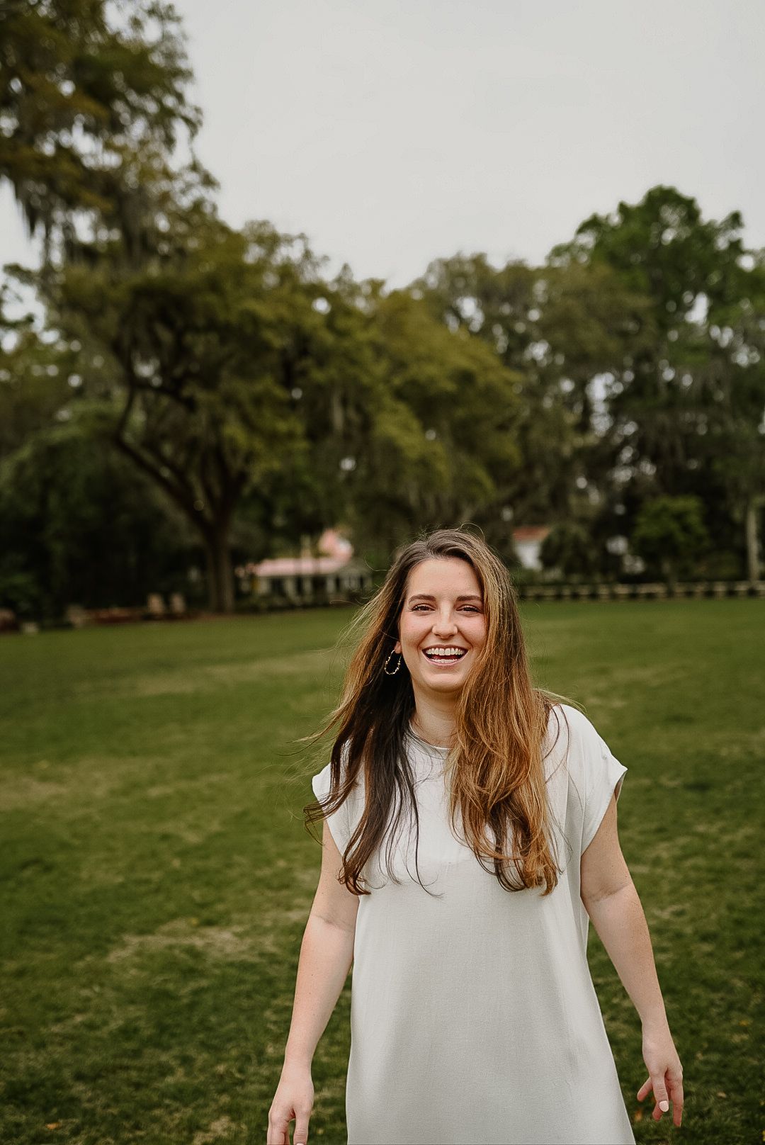 A woman in a white dress is standing in a grassy field.