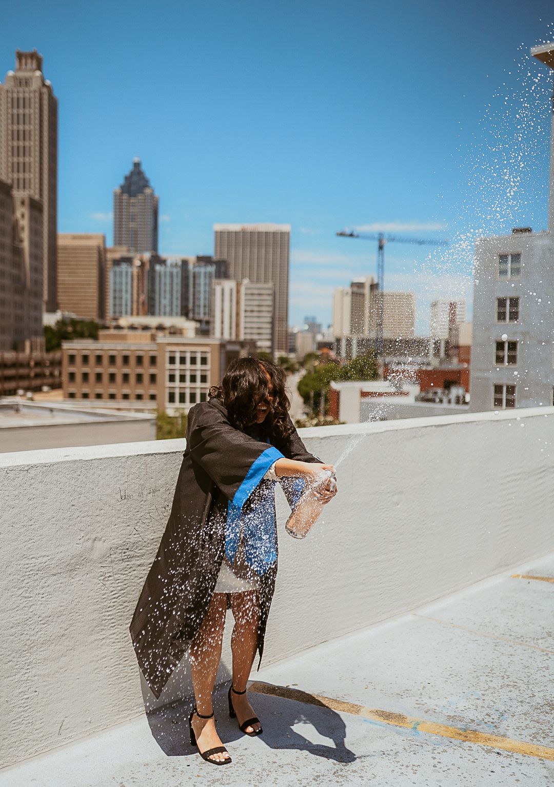 A woman in a graduation cap and gown is standing on a rooftop in front of a city skyline.