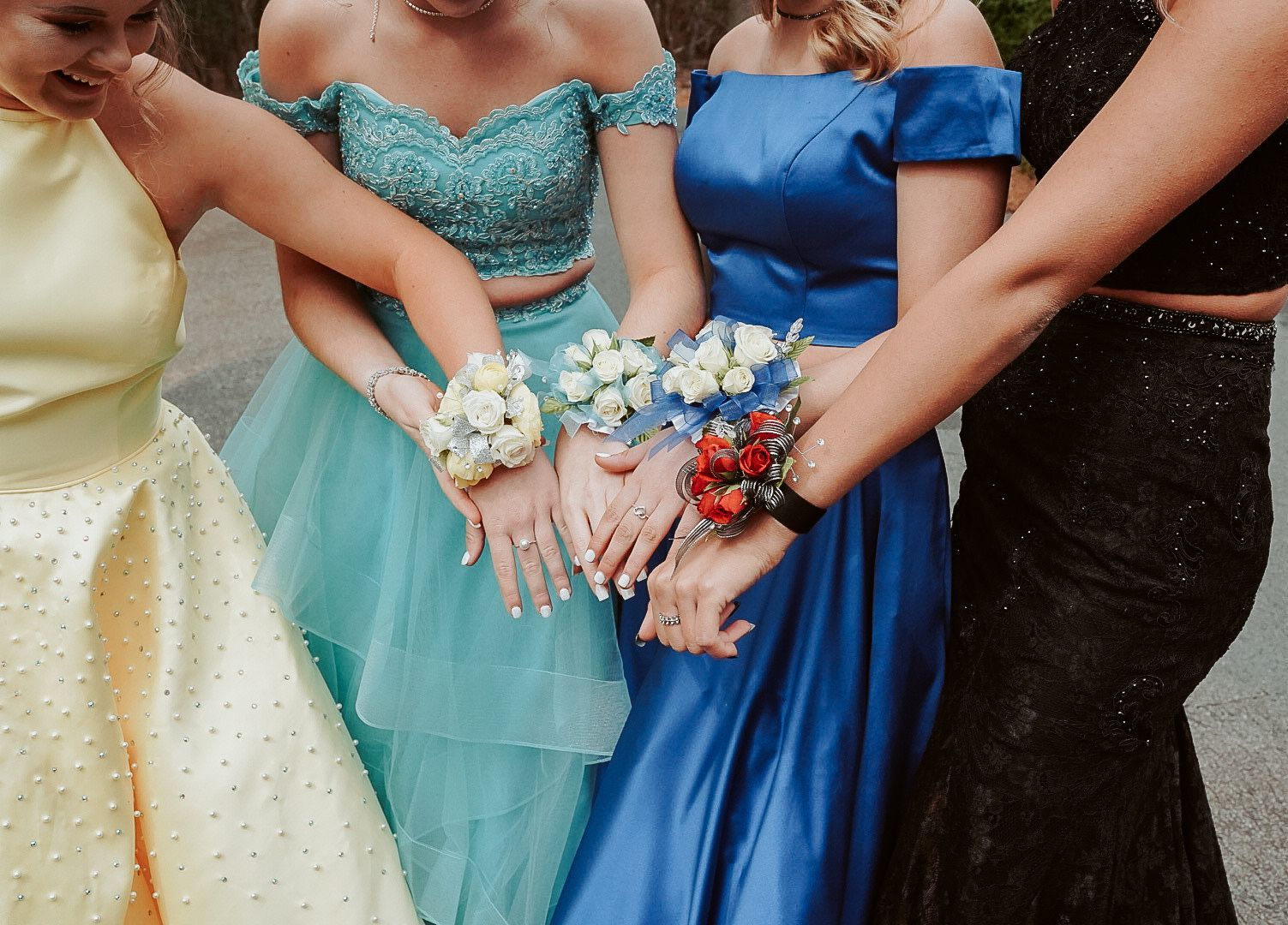 A group of girls in prom dresses are holding hands