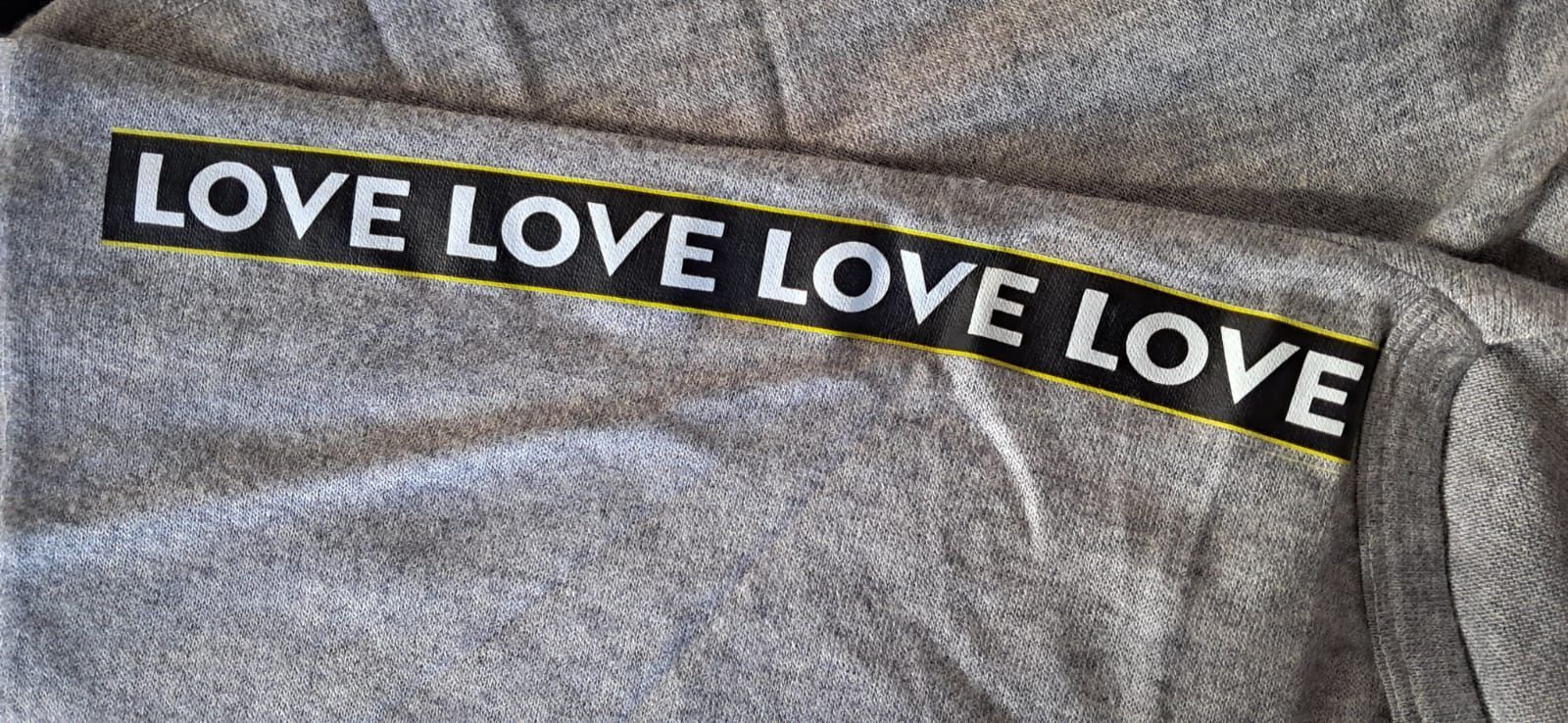 Un suéter negro con la palabra amor en las mangas está colgado en una percha de madera.