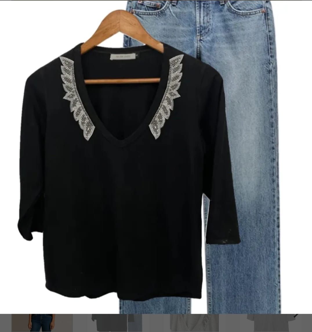 Una camisa negra con cuello de encaje cuelga de una percha de madera.