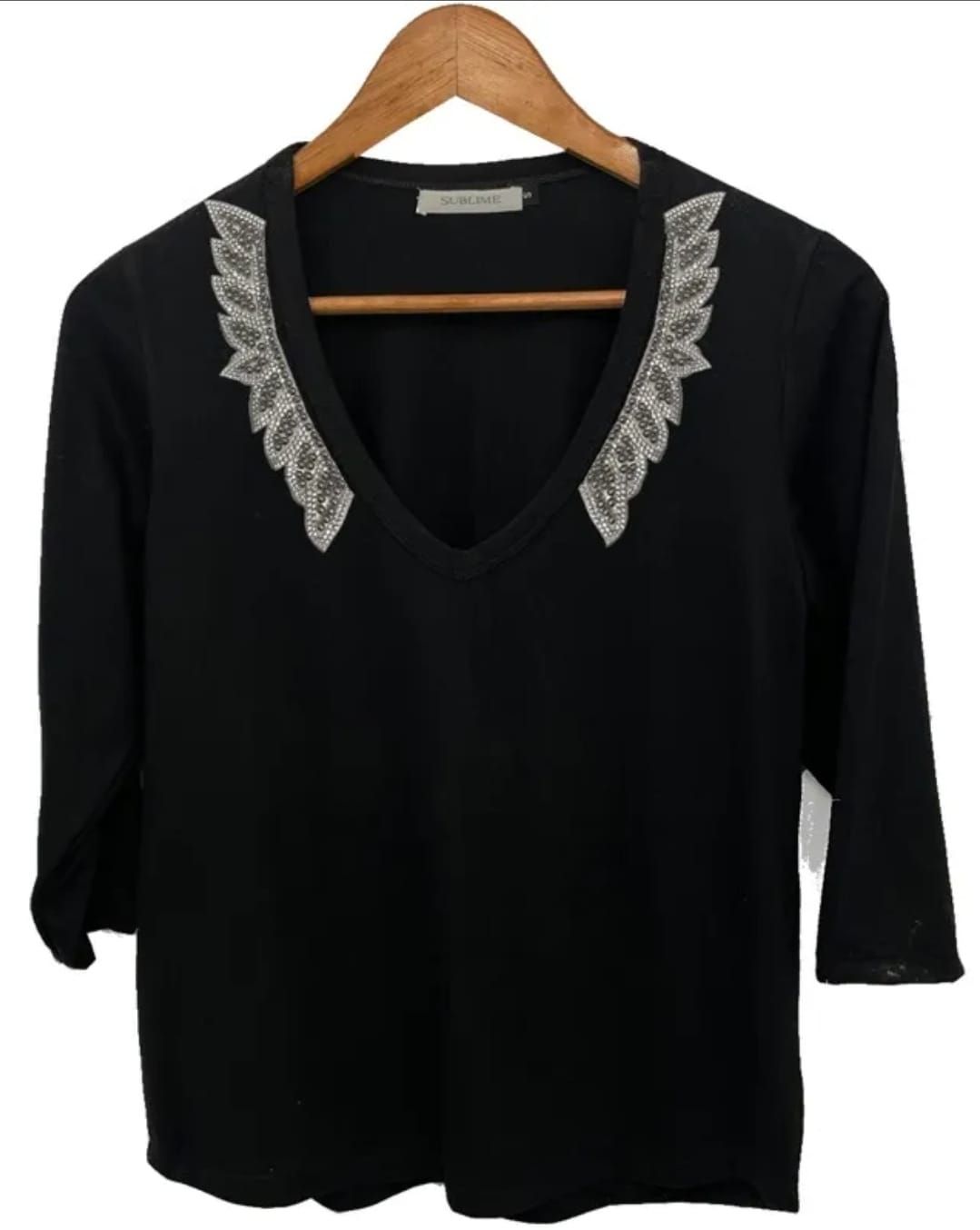 Una camisa negra con cuello de encaje cuelga de una percha de madera.