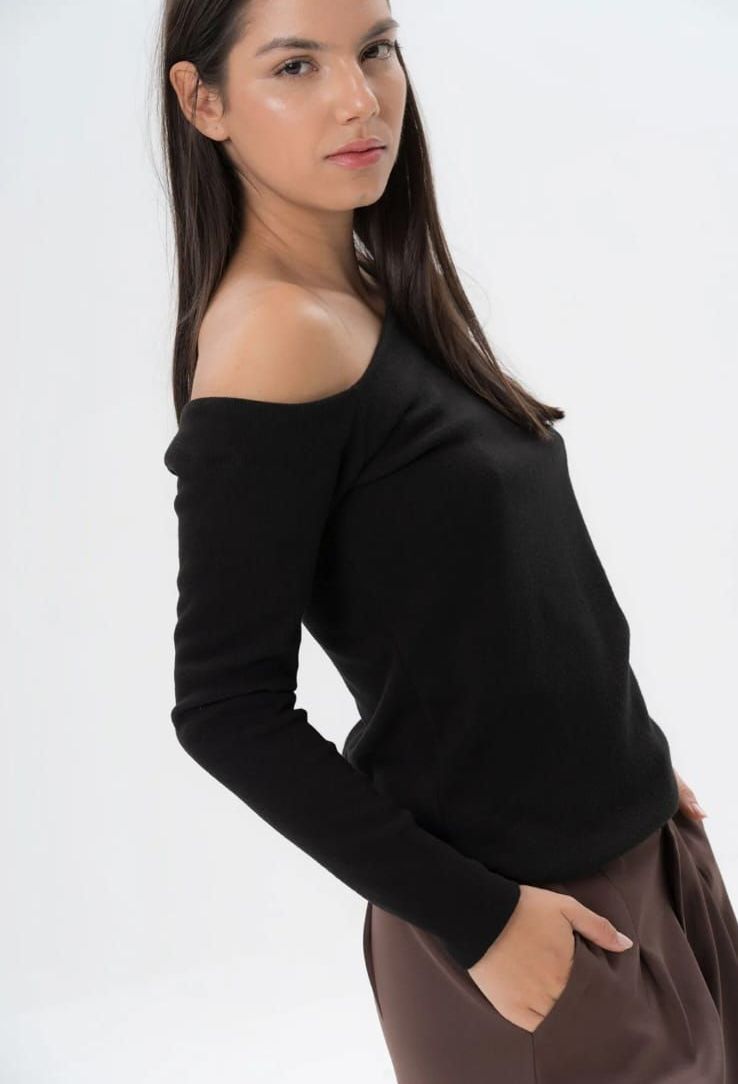 Una mujer lleva una blusa negra con hombros descubiertos y pantalones marrones.