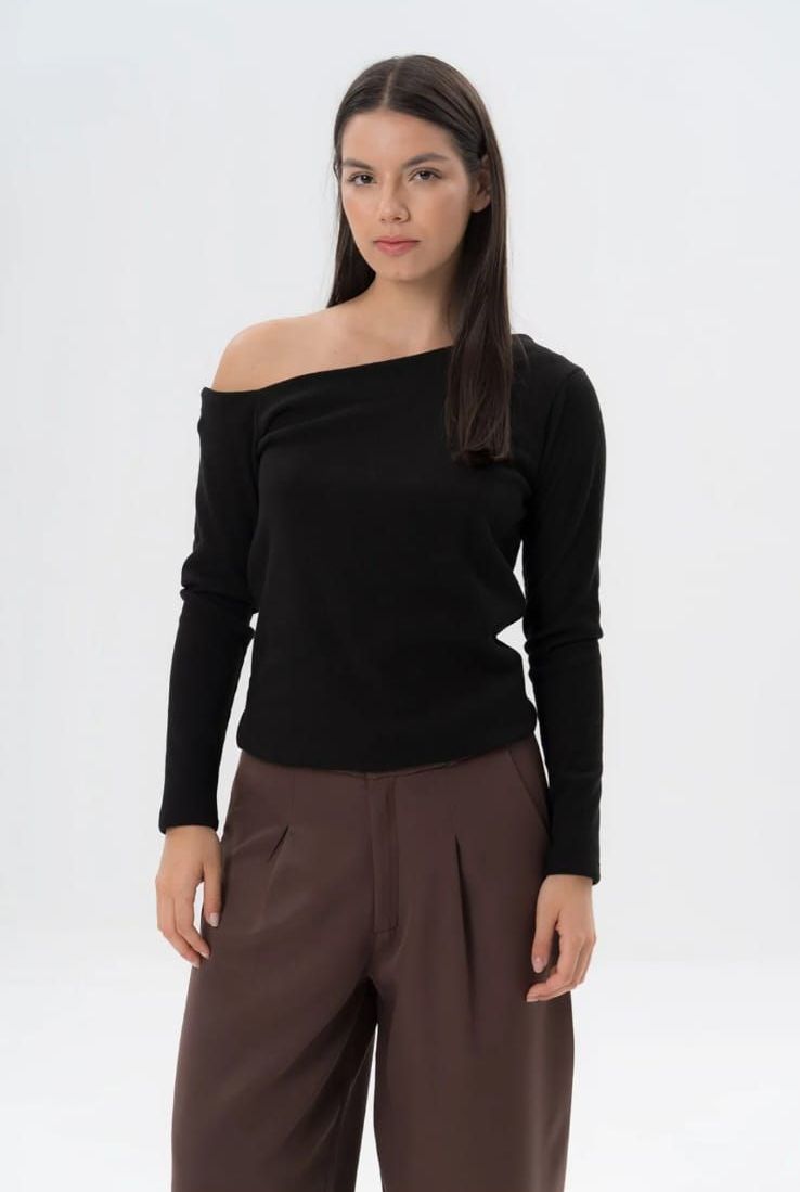 Una mujer lleva una blusa negra con hombros descubiertos y pantalones marrones.