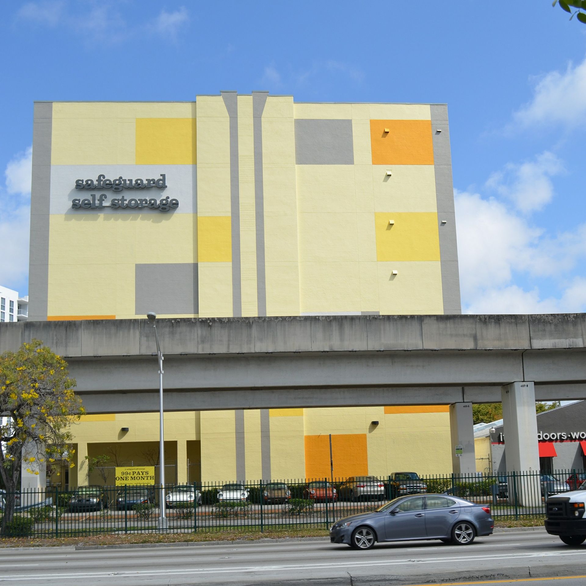Safeguard self storage building; large, yellow, under highway, parked cars, sunny day.