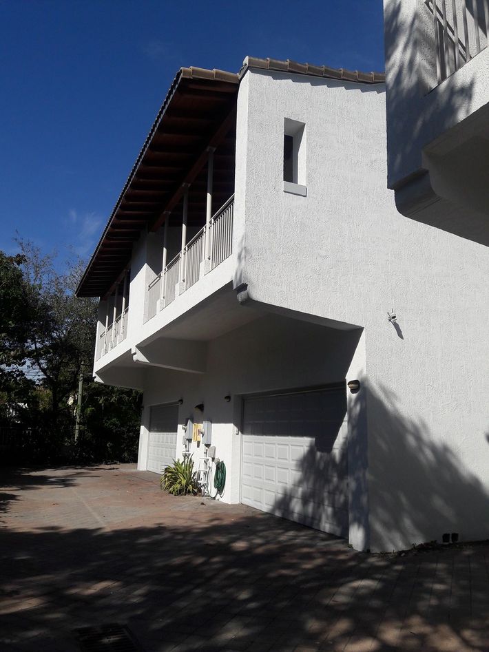 White stucco house with balcony over two garages; sunny day.