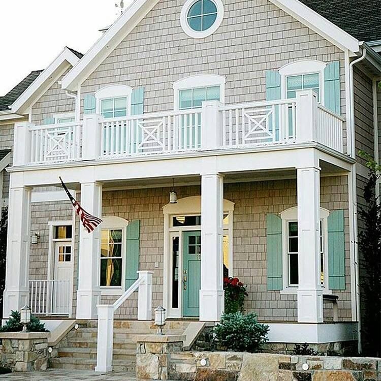Two-story house with gray shingles, turquoise shutters, balcony, white trim, and an American flag.