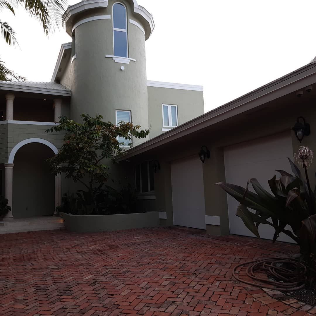 Green stucco house with brick driveway and a turret.