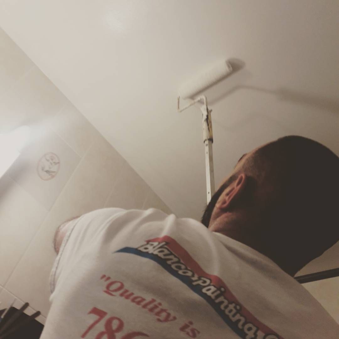 Person in white shirt painting a ceiling with a roller.