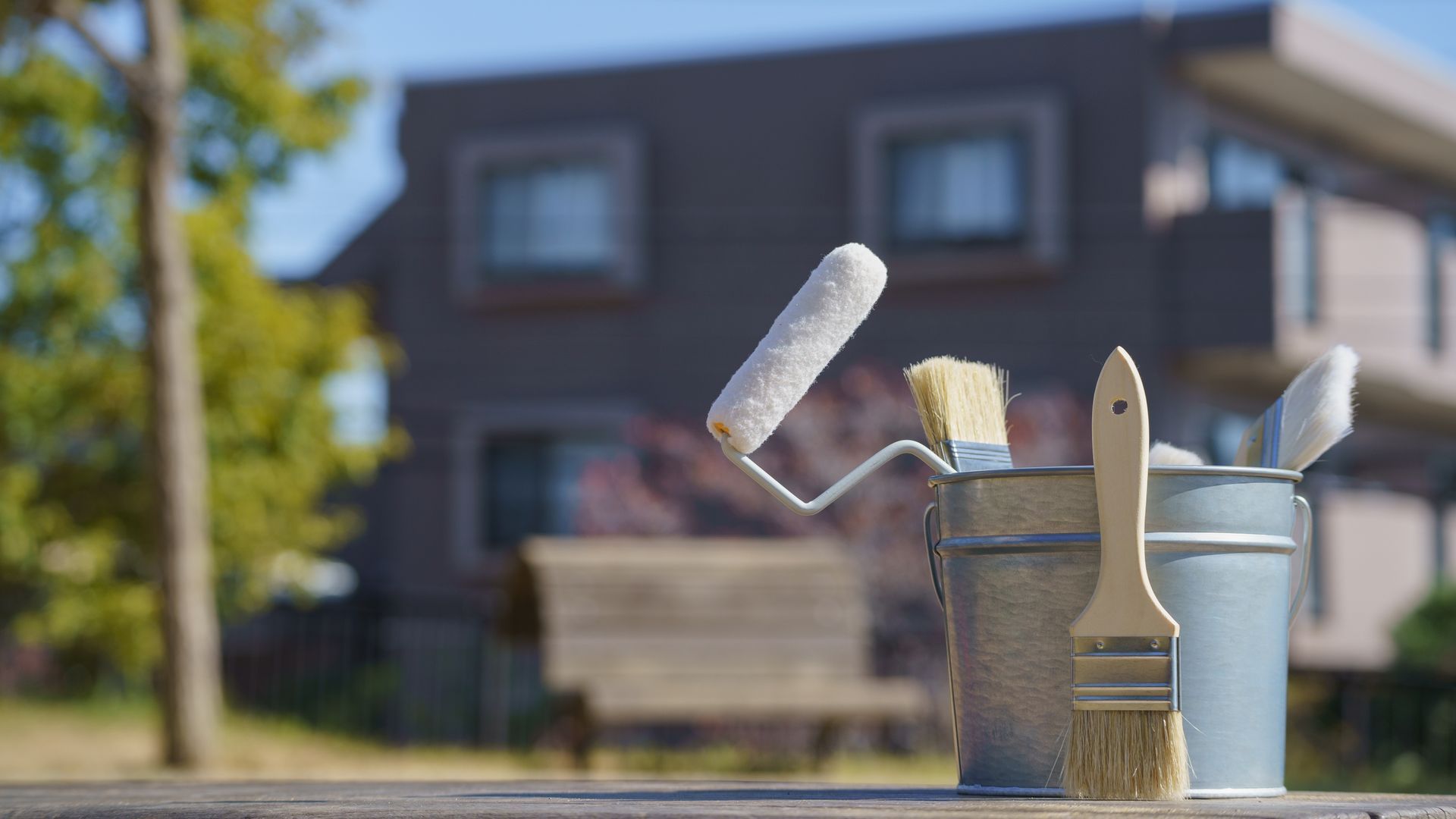 Paint supplies, including a roller and brushes, on a table in front of a house.