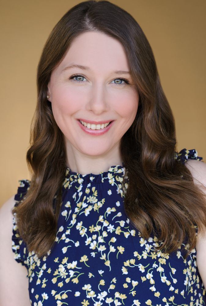 A woman is sitting at a desk with a laptop and a vase of flowers.