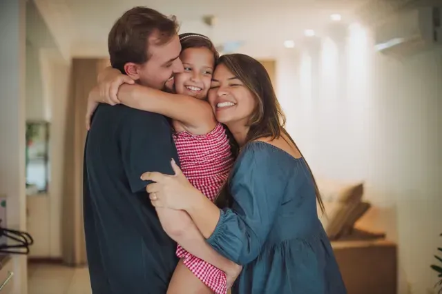 A man and woman are hugging a little girl in a living room.