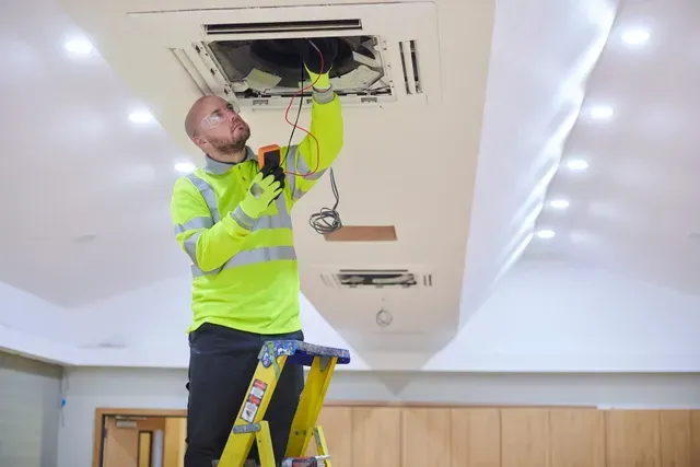 A man is inspecting an AC in an office.