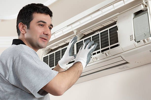 A technician with gloves working on an AC unit, delivering expert emergency AC repair service.