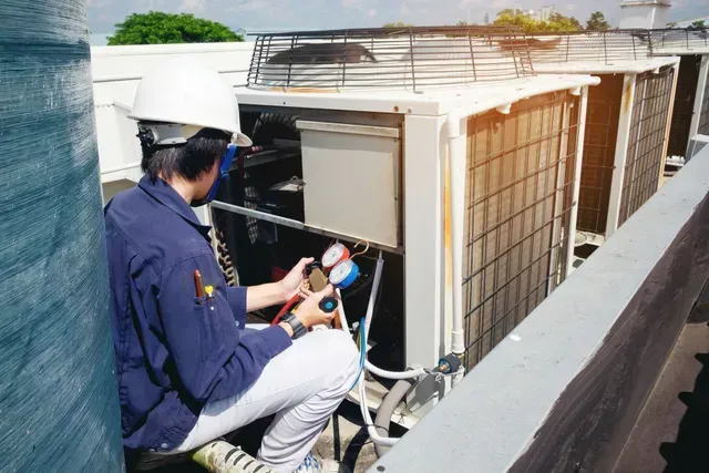 HVAC technician performing air conditioning unit maintenance with pressure gauges outdoors.
