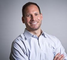 A smiling doctor in a lab coat with a stethoscope around his neck.