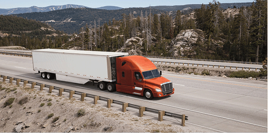 A red semi truck is driving down a highway with mountains in the background.