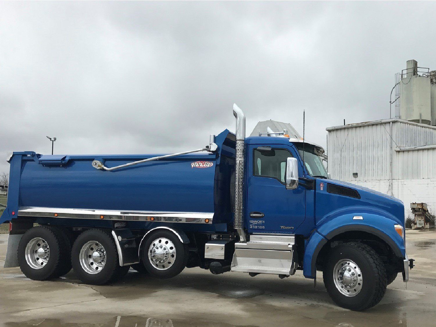 A blue dump truck is parked in front of a building.