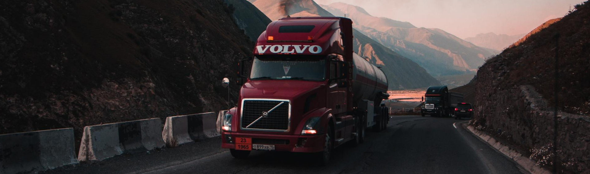 A red volvo semi truck is driving down a mountain road.