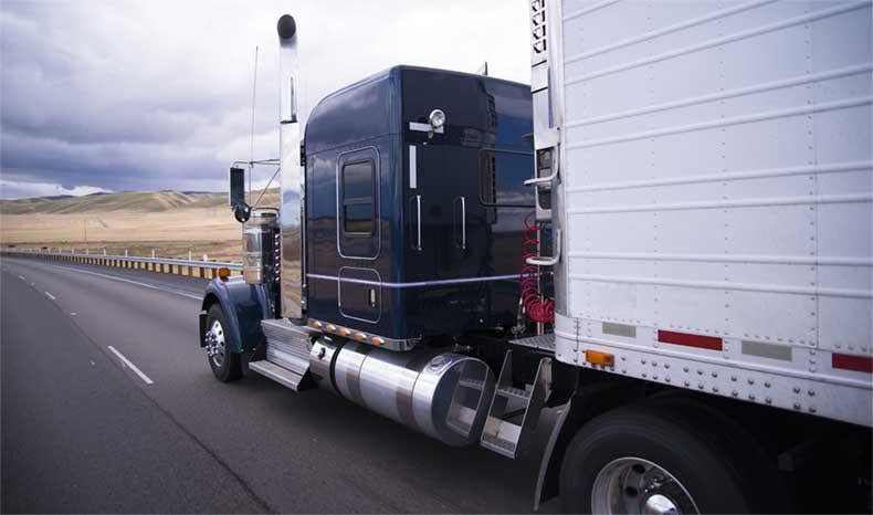 A semi truck with a white trailer is driving down a highway.