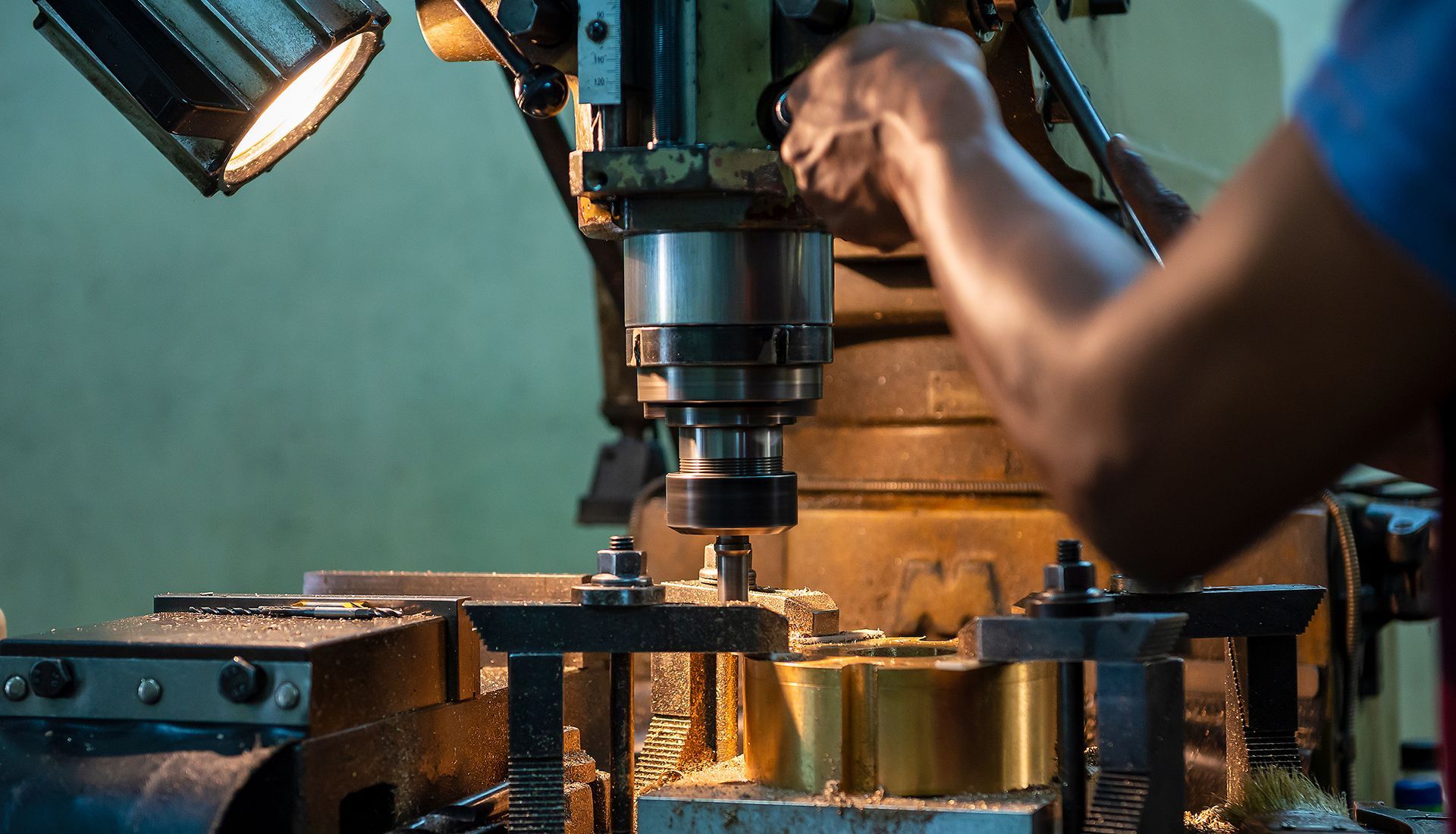 Person operating a milling machine in a workshop, working on a metal component.