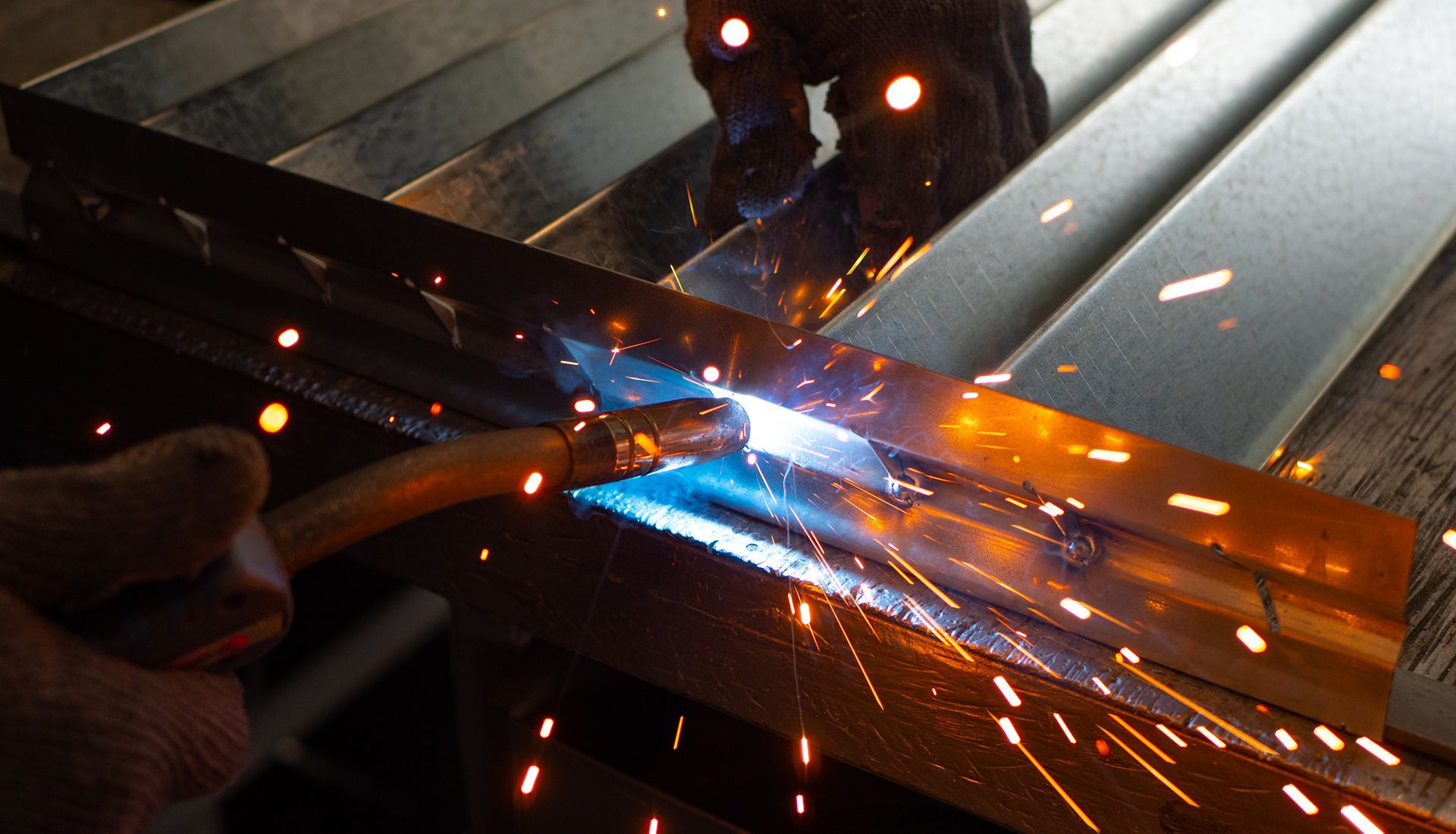 Welder working on metal, creating sparks and a bright blue light.