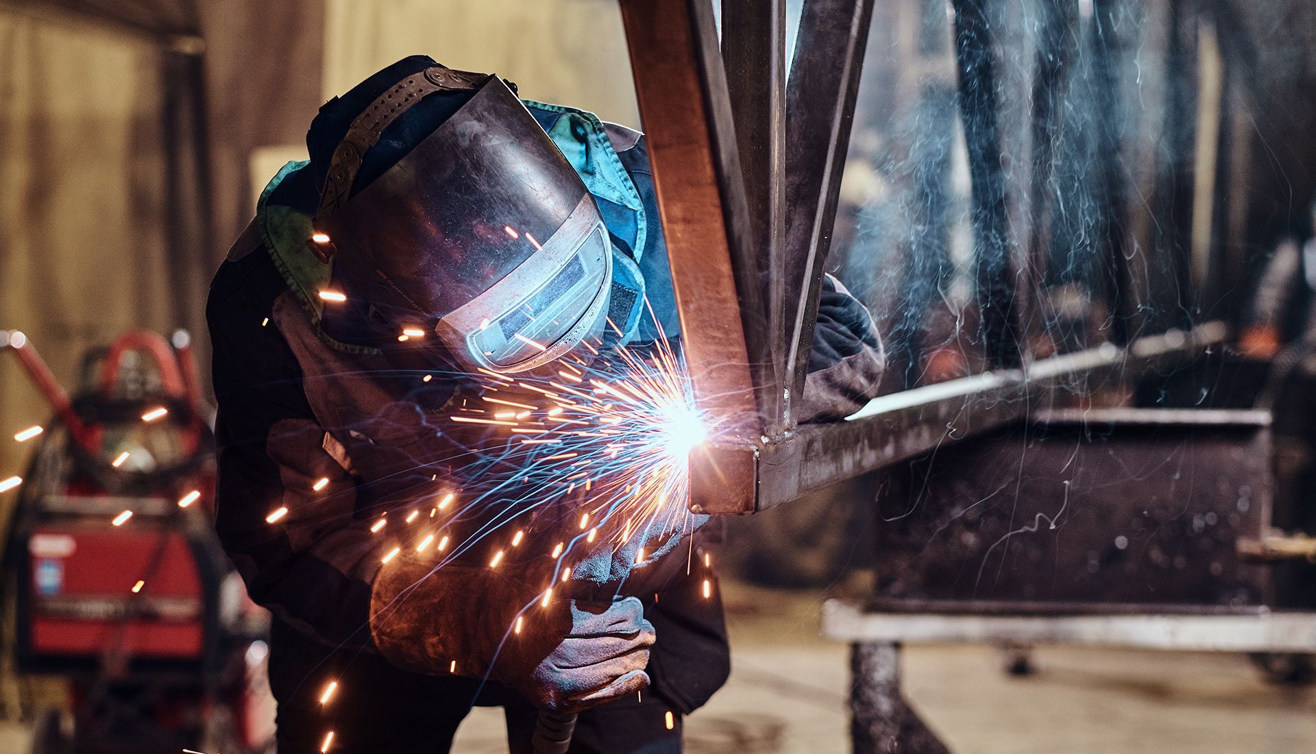Welder in a workshop, sparks flying as they join metal beams with a bright welding torch.