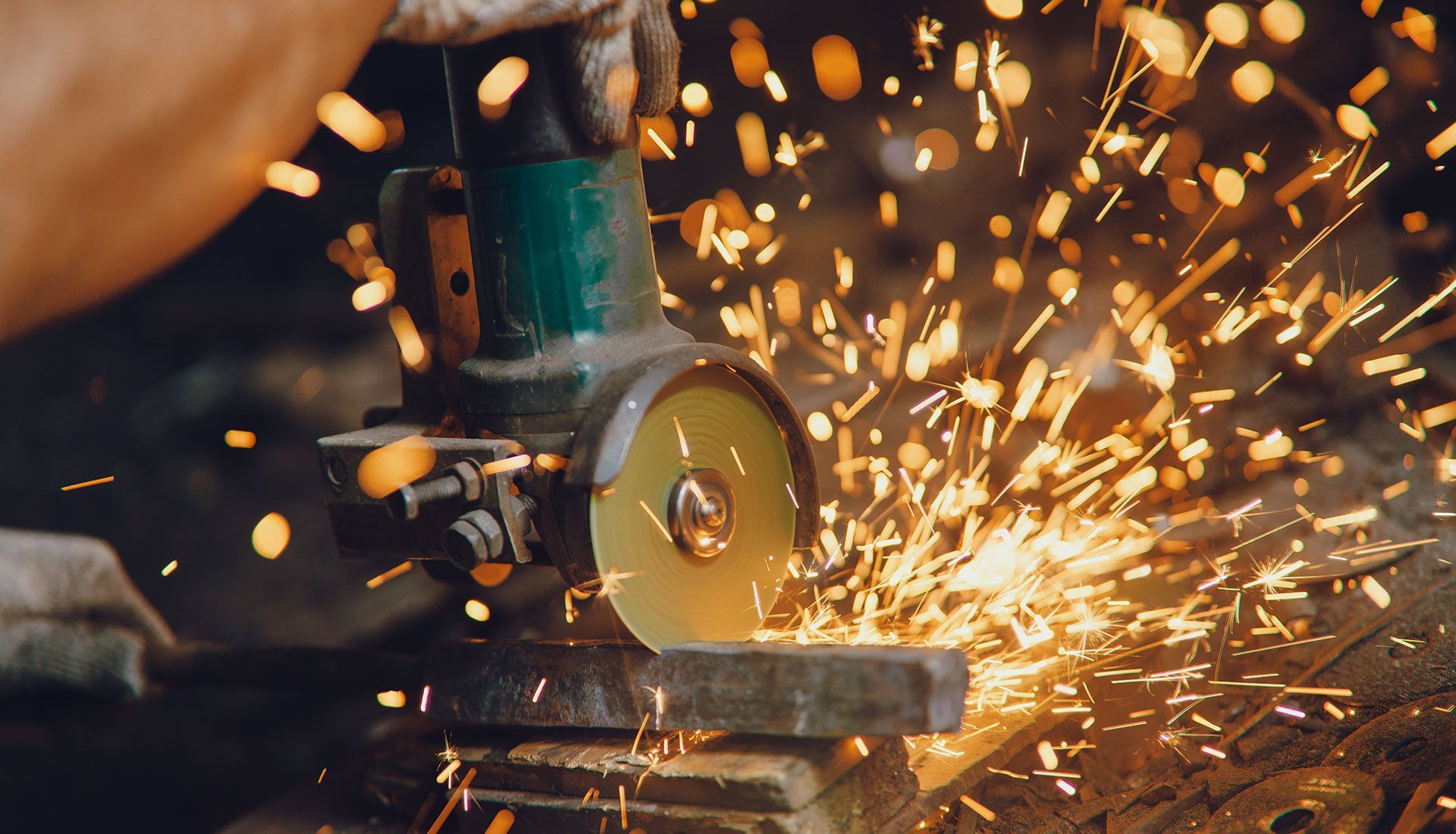 A person using a grinder, creating sparks while cutting metal.