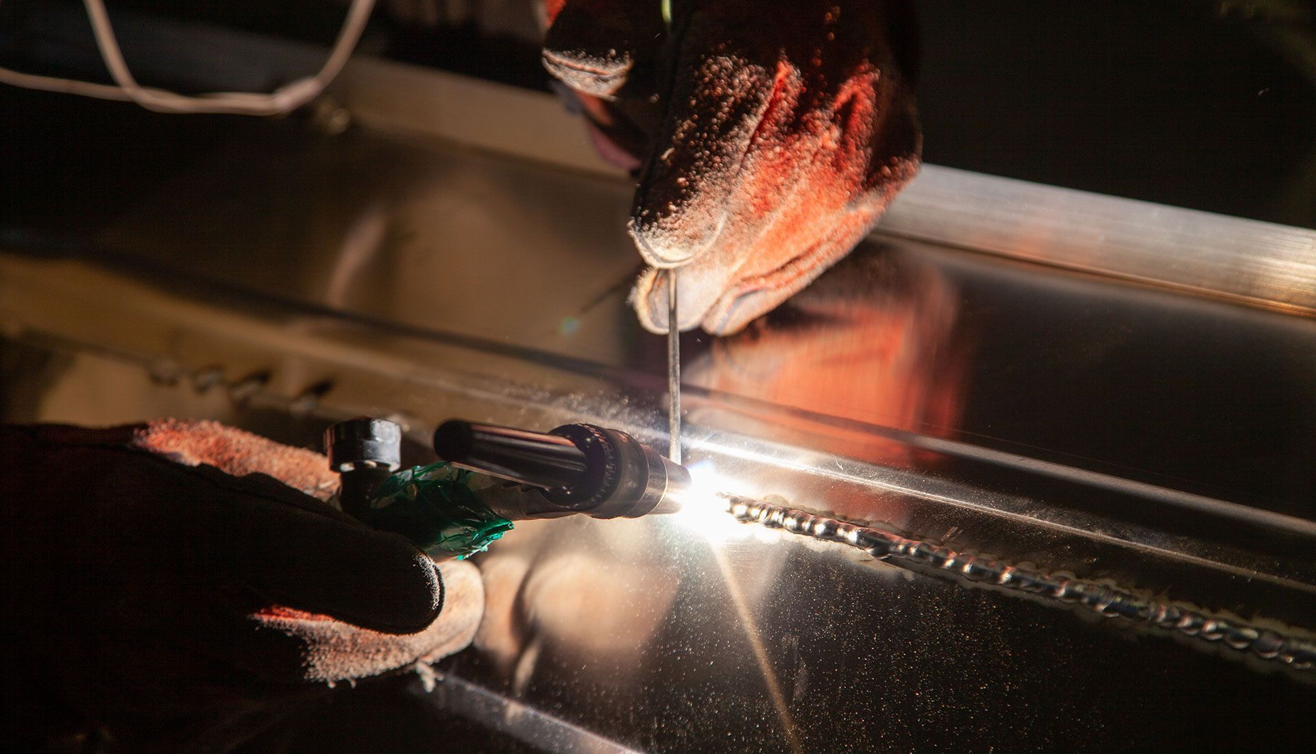 Welder in protective gloves welding metal; sparks fly.