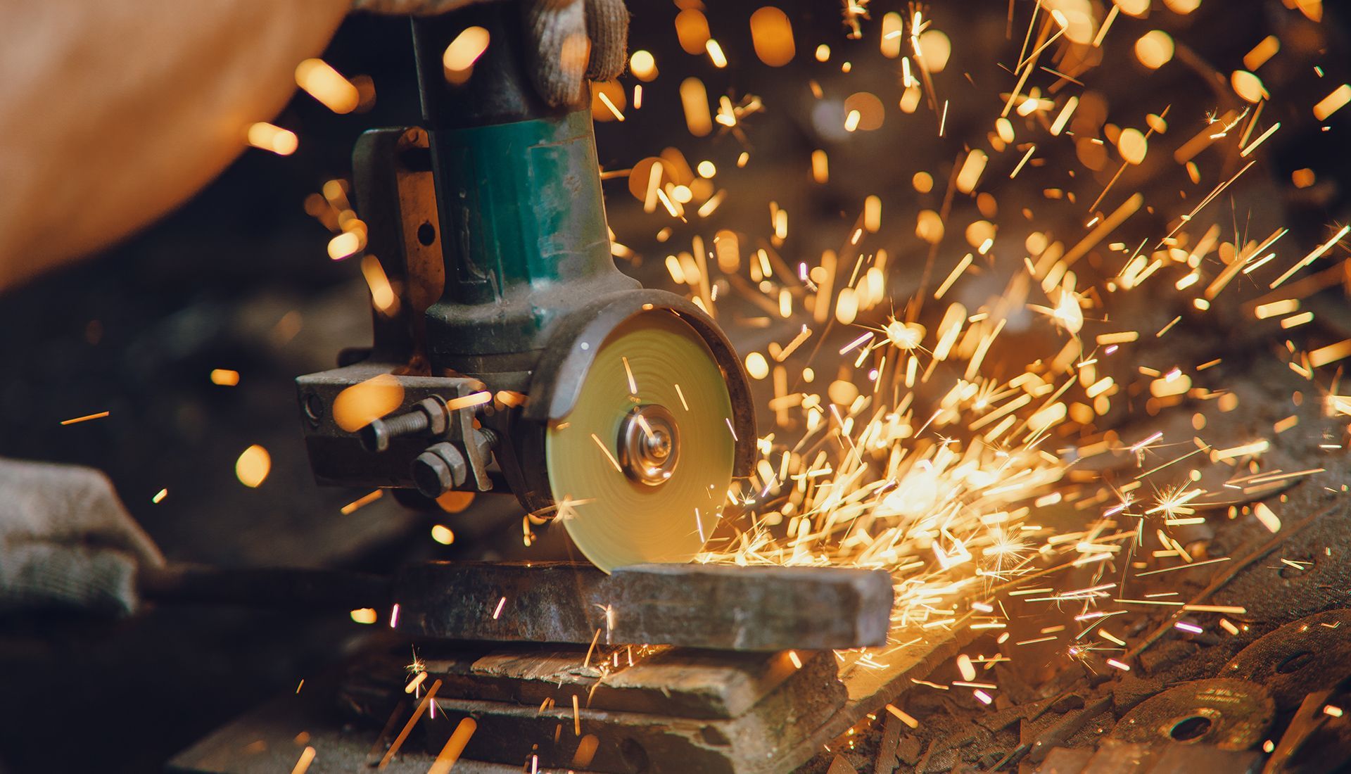 A person uses an angle grinder, creating sparks while cutting metal in a workshop.