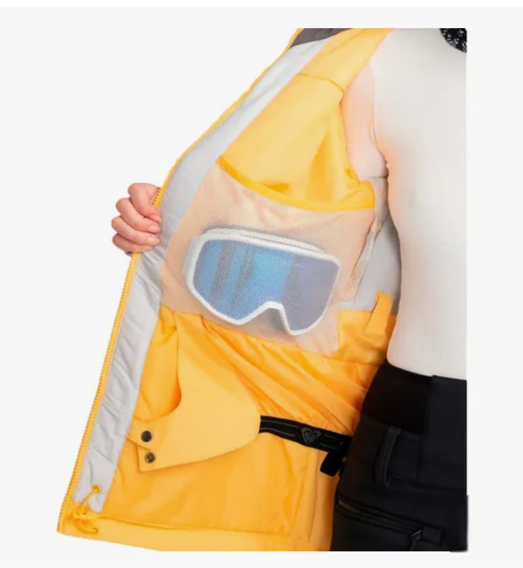 Mujer con chaqueta de esquí amarilla, de pie frente a un fondo blanco.