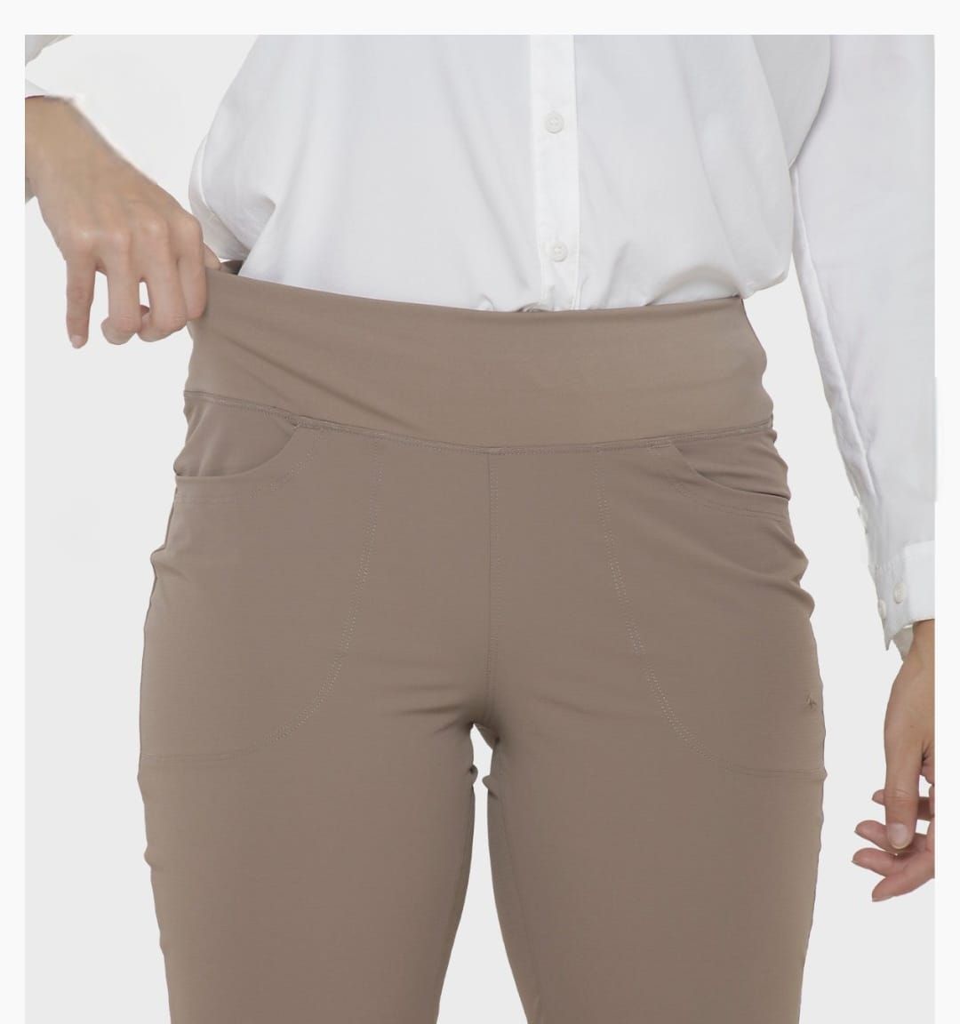 Pantalones color beige sobre una persona que lleva una camisa blanca y zapatos negros, de pie en el interior.