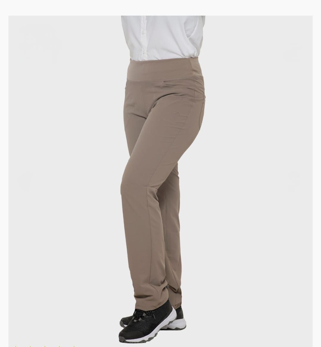 Pantalones color beige sobre una persona que lleva una camisa blanca y zapatos negros, de pie en el interior.