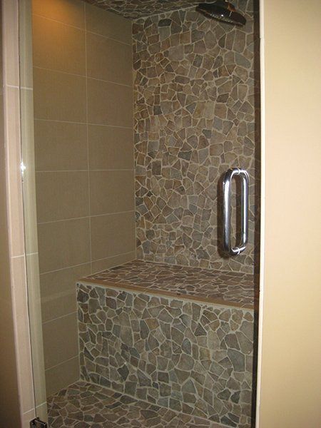 A walk in shower with a stone bench and a glass door.