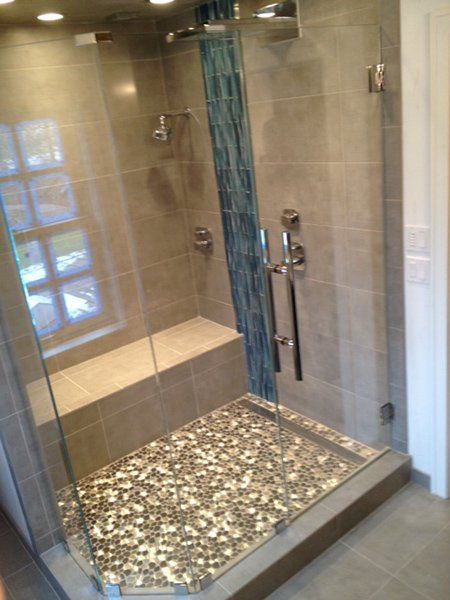 A bathroom with a walk in shower with a bench and a glass door.