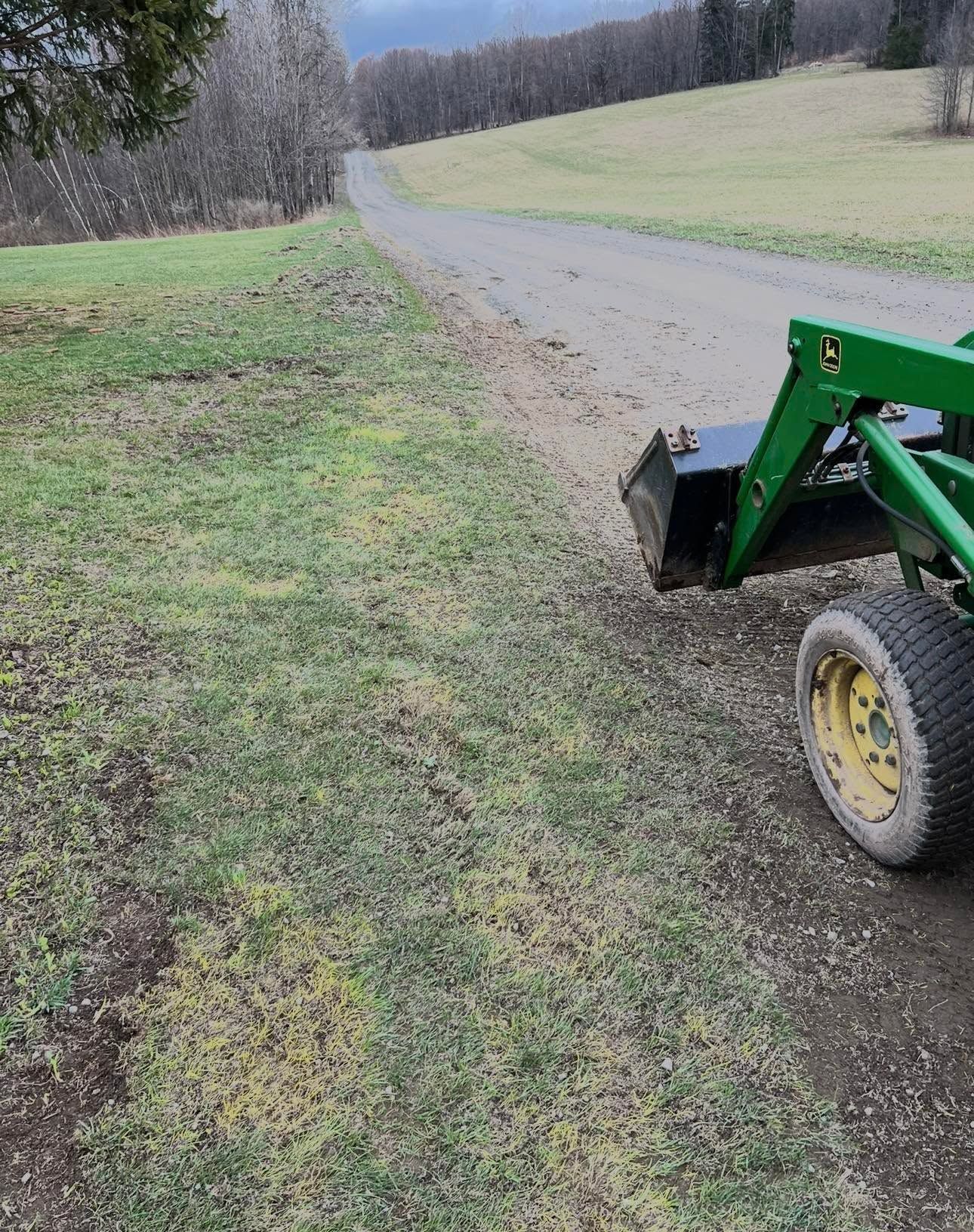 Green tractor on a grassy edge beside a curving gravel road in a rural field.