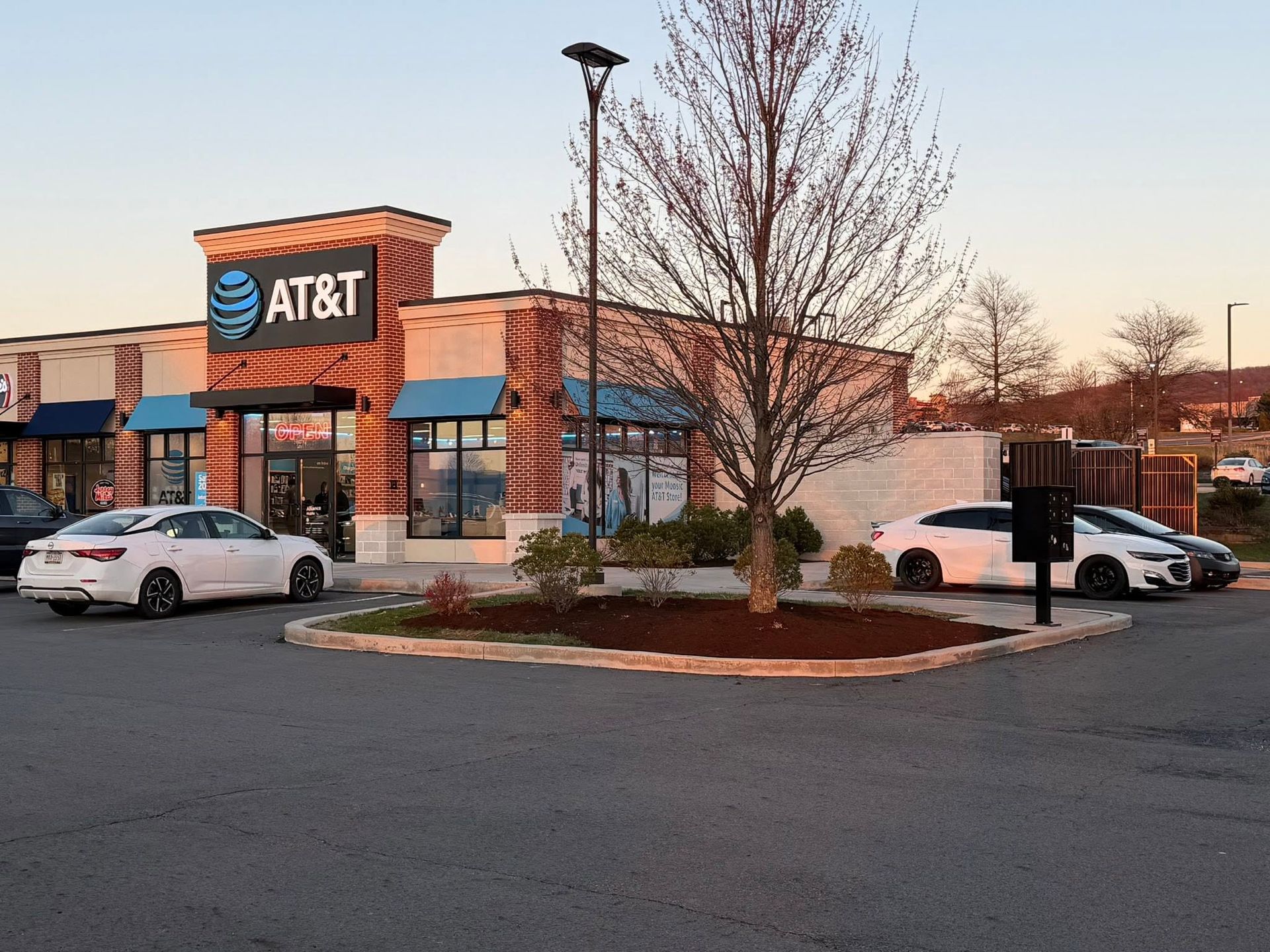 AT&T storefront at dusk with parked cars and bare trees in a lot