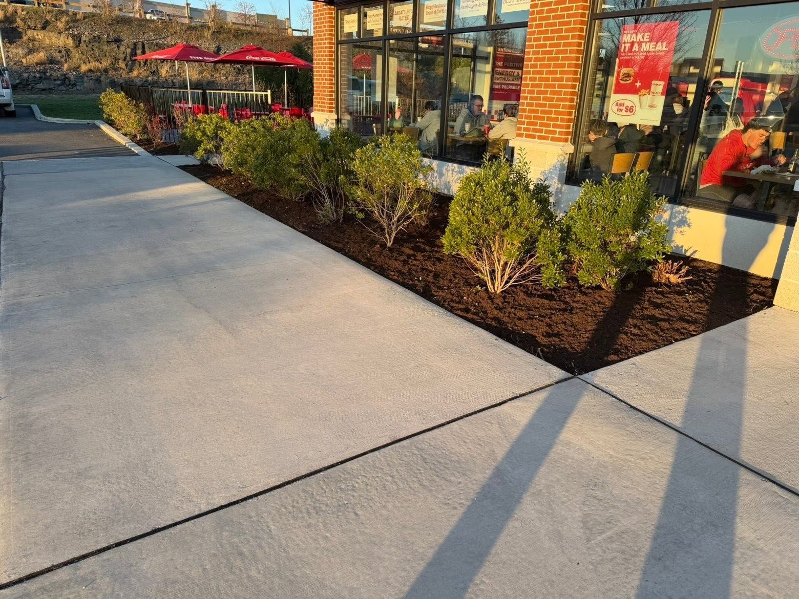Storefront sidewalk with landscaping, bushes, and long shadows in the afternoon sun