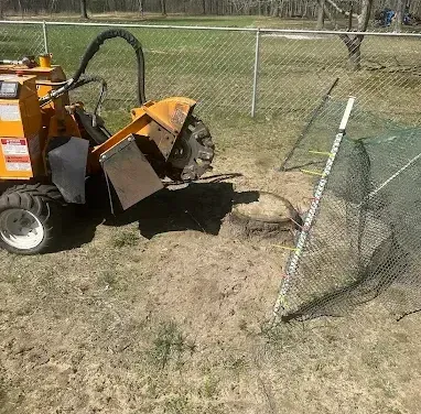 A stump grinder is sitting in the dirt next to a chain link fence.