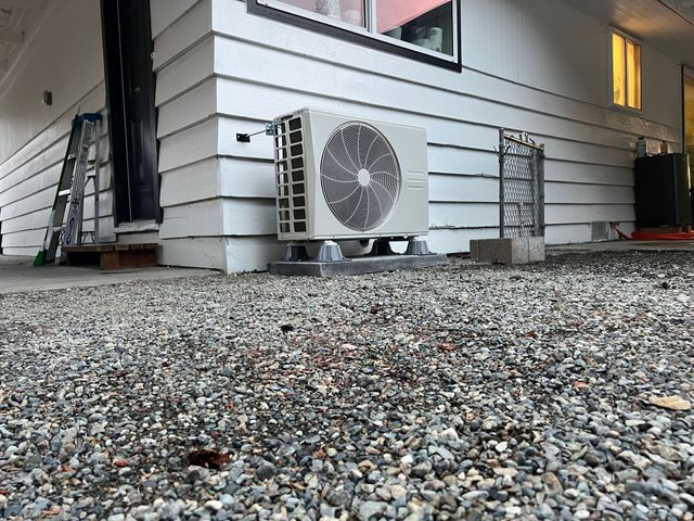 Exterior HVAC unit mounted on concrete pad near a white house with gravel ground.