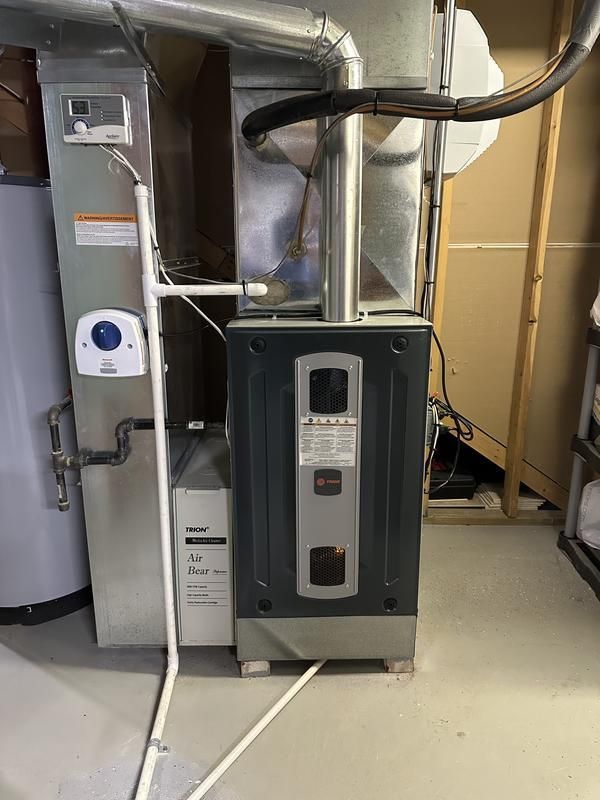 An air conditioner is sitting in a basement next to a water heater.